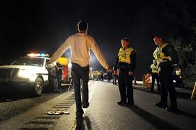 A person performs a sobriety test on a road at night, observed by three police officers and a police car with flashing lights, while the nearby Law Office of Kevin Bessant oversees the procedure.