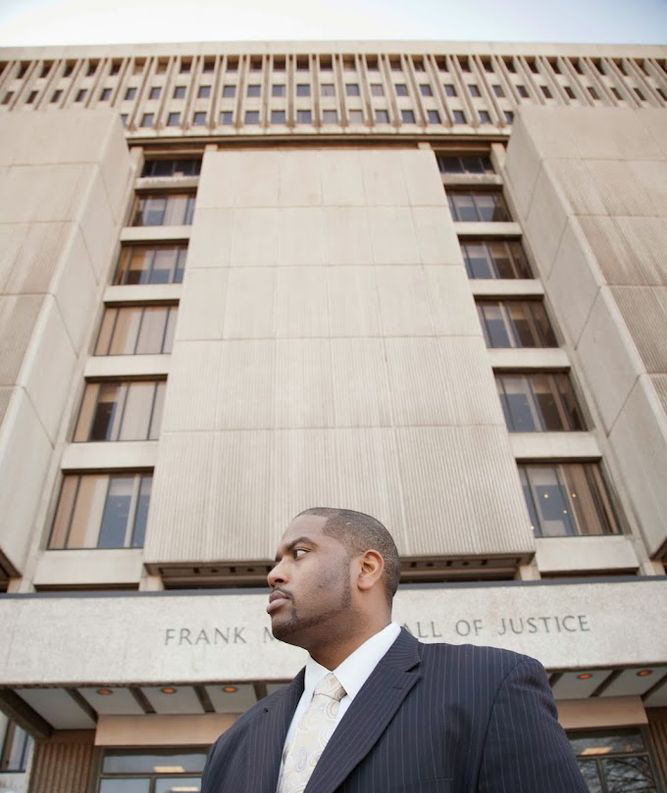 A man in a suit stands in front of a large building labeled "FRANK M...", embodying the professionalism and dedication of a top-tier Detroit Criminal Defense Attorney.